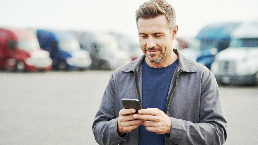 Truck driver using a mobile phone beside a semi-truck.