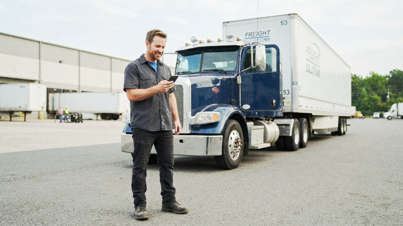 Truck driver using a mobile phone beside a semi-truck.