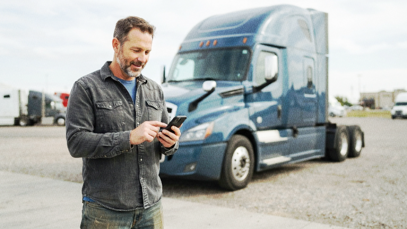 Truck driver using a mobile phone beside a semi-truck.